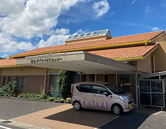 介護施設の建物外観。駐車場に送迎用の白い車が停められている