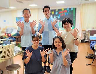 スタッフと入居者が一緒に手を上げて笑顔でポーズをとるレクリエーション風景